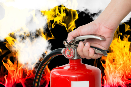 Closeup of hand handle fire extinquisher in flame of fire and smoke backgroundの写真素材