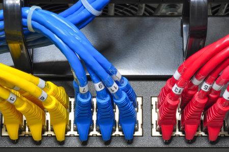 Colored ethernet cables in yellow, blue, and red are plugged into cable management patch panel of a...