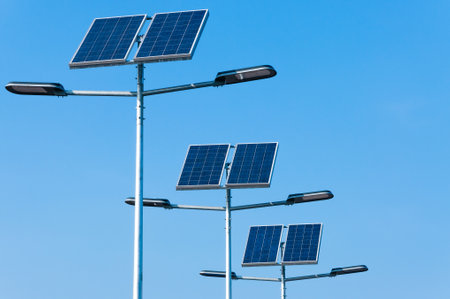 Multiple streetlights equipped with solar panels in clear blue sky background, showcasing renewable...