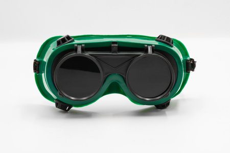 Close-up front view of welding goggle features a green frame and black lenses, designed for eye protection while welding. Isolated on white background.の写真素材
