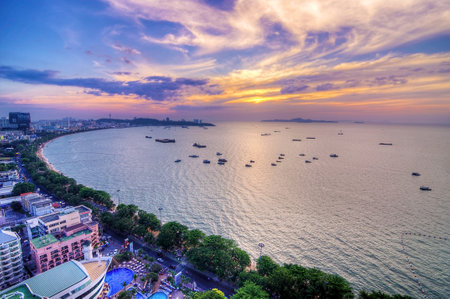 Golden hues blend with purple and blue as the sun sets over the bay, casting reflections on the water alongside a lively coastal area.の写真素材