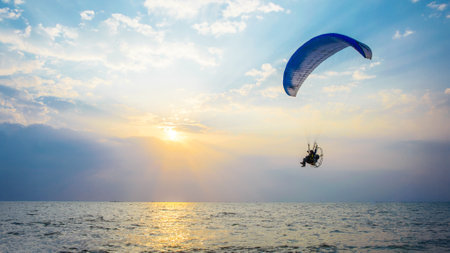 A person paraglides above the calm ocean waters at sunset, enjoying the serene views and fresh air.の写真素材