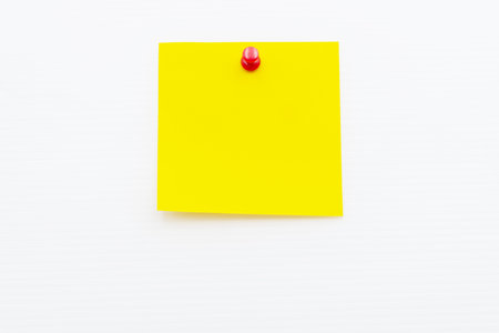 A vibrant yellow post note paper is secured with a red push pin against a plain white background, suitable for jotting down reminders.の写真素材