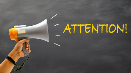 A person holds a megaphone, calling for attention with a message on a dark chalkboard during an outdoor gathering.の写真素材