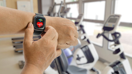 A person checks a smartwatch heart rate monitor while exercising at a modern gym, tracking fitness...