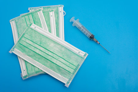Face masks and a syringe on a blue background for health safety measures in vaccination campaigns