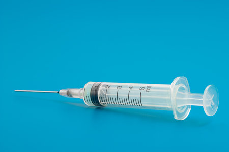 A medical syringe is lying on a solid blue background, showcasing its scale and sharp needle, used for injections or drawing fluids.の写真素材
