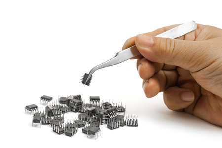 A hand carefully uses tweezers to pick up a small integrated circuit from a larger pile of...