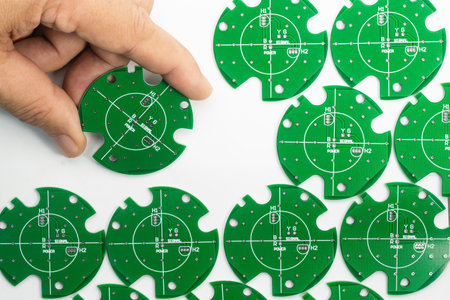 A hand carefully places a green circuit board piece among others, showcasing precision and detail in...