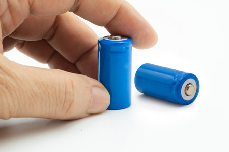 A hand is reaching for a blue lithium ion battery while another similar battery sits on a white...