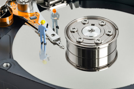 Two miniature engineers inspect components of a hard disk drive in a modern technology workspace,...
