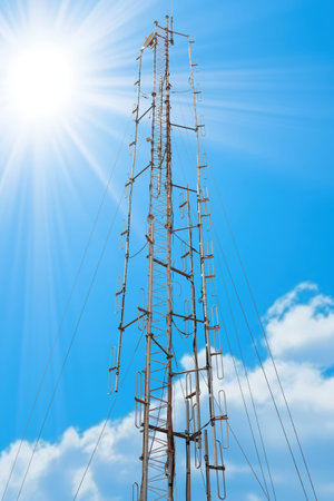 A tall antenna tower reaches towards a clear blue sky, illuminated by bright sunlight, highlighting...