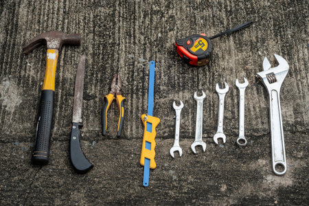 A collection of hand tools laid out on concrete, including a hammer, pliers, and wrenches, ready for repair tasks.の写真素材