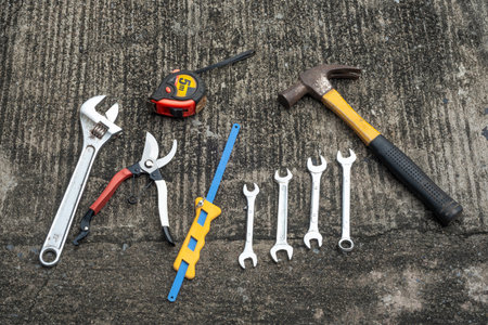 Various hand tools, including pliers, wrenches, and a hammer, are arranged neatly on a concrete surface, ready for use in tasks.の写真素材
