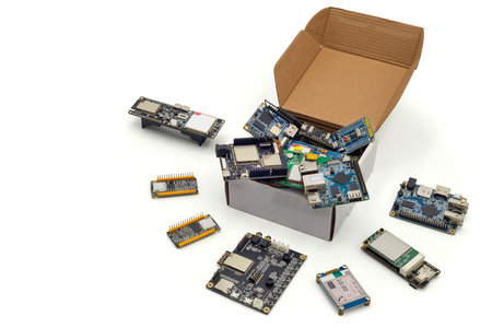 Various IoT and embedded development boards scattered from an open box on a white background,...