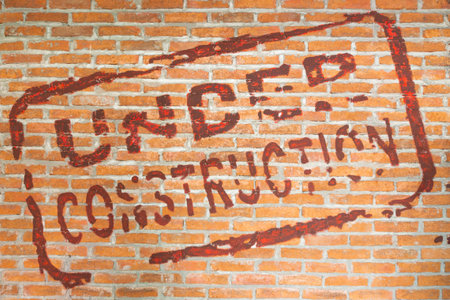 Red painted under construction text on brick wall representing renovation, urban development, transition, and temporary disruption in construction or rebuilding projects.の写真素材