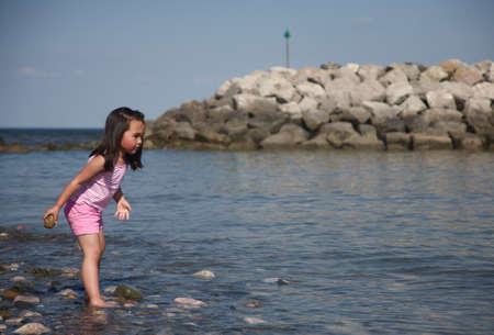 Stone throwing little girl on the beach  の写真素材