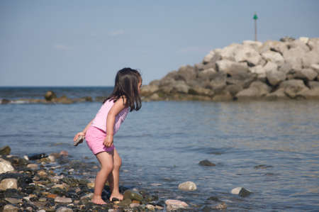 Stone throwing little girl on the beach  の写真素材