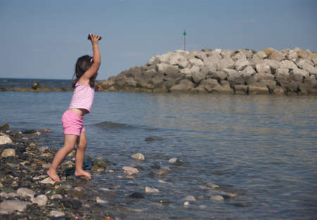 Stone throwing little girl on the beach. の写真素材