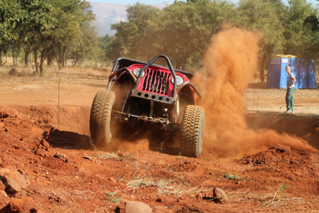Rustenburg, South Africa - JUNE 17, 2017: National Extreme Modified 4x4 Vehicle Championship. Red Car climbing out steep dugout, front wheels suspended, kicking up sand and dust.のeditorial素材