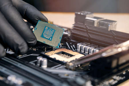 Engineer repairman holding hands in black gloves chip processor CPU to insert into the socket of the...
