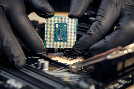 Engineer repairman holding hands in black gloves chip processor CPU to insert into the socket of the...