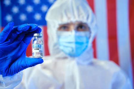 Blured doctor or nurse wearing personal protective equipment and holding syringe of corona covid-19...