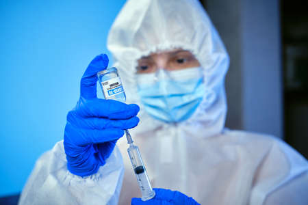 Blured doctor or nurse wearing personal protective equipment and Gathers the vaccine from the ampoule with a syringe of corona covid-19 vaccine in laboratory or hospital.の写真素材