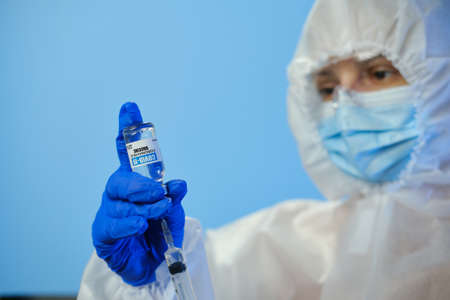 Blured doctor or nurse wearing personal protective equipment and holding syringe of corona covid-19 vaccine in laboratory or hospitalの写真素材