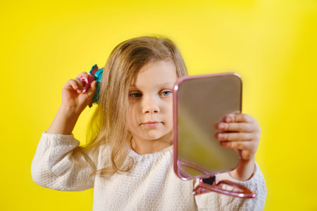 Adorable little girl holding pocket mirror standing on yellow backgroundの写真素材