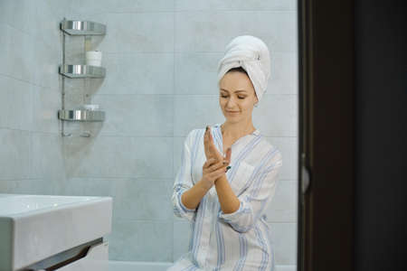 Woman in bathrobe applying moisturizing hand cream, in the bathroom. Skin careの写真素材