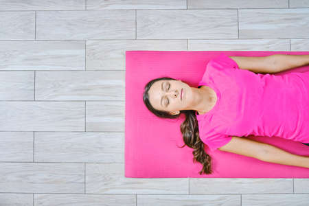 Yoga at home concept. Attractive young woman doing yoga exercises lying on the floorの写真素材