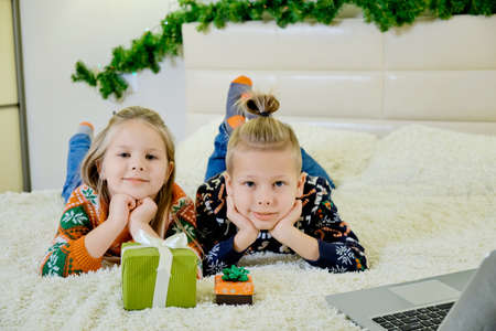 New Years concept, children lie on the couch in Christmas clothes, and make an online call on a...
