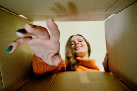 Young woman carefully opens box delivery from online store. Coronavirus pandemic quarantine, inside of carton box bottom view. Blurred faceの写真素材