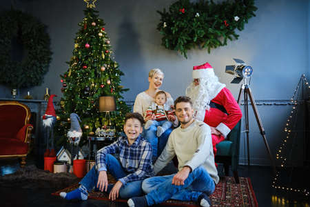 family together with santa claus sitting on sofa and floors and looking at camera.