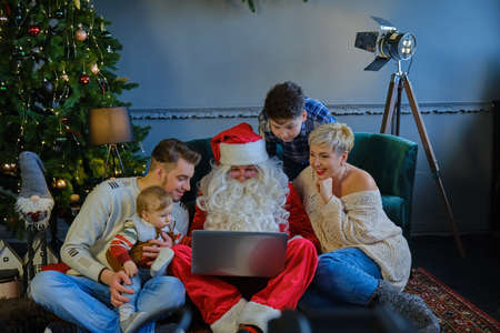 family together with santa claus sitting on sofa and floors and looking at laptop.の写真素材