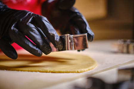 Female hands in black gloves making a cookie using a metal mold cut out the dough.