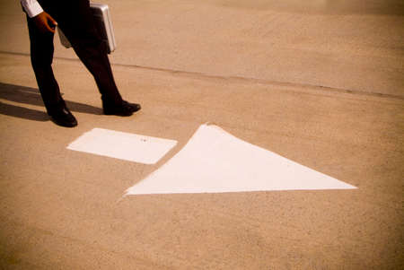 business man standing in front of arrow on parking lotの写真素材