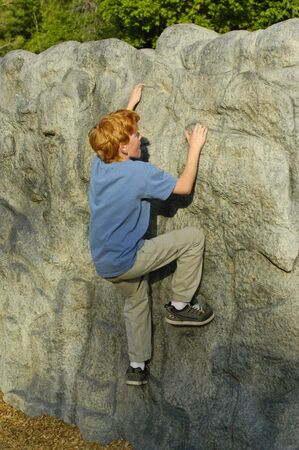 10 year old boy climbing man-made rock wall at park                               の写真素材