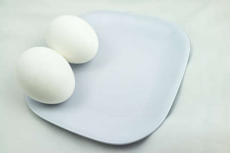 Two Whole Eggs Resting on Each Other On White Plate With White Backgroundの写真素材