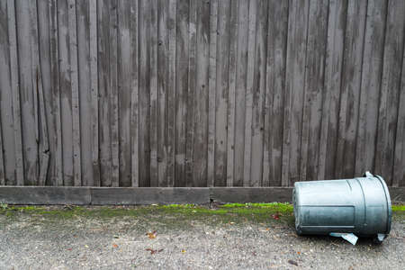 Grey and Gloomy Wooden Fence with Tipped Over Garbage Can in Frontの写真素材