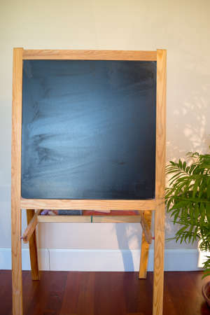 Small Wooden Chalk Board Stand Against Off White Wall With Half Plantの写真素材