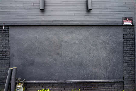 Grey/black brick and wood wall with gas meter and lights and no trespassing signの写真素材