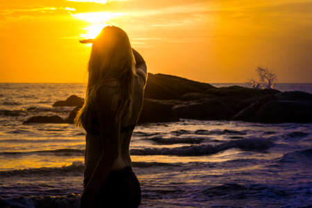A female surfer chick looks out to the ocean and watches the sunset while on a tropical holidayの写真素材