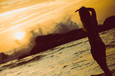 A female stands in the ocean as waves crash against the rocks