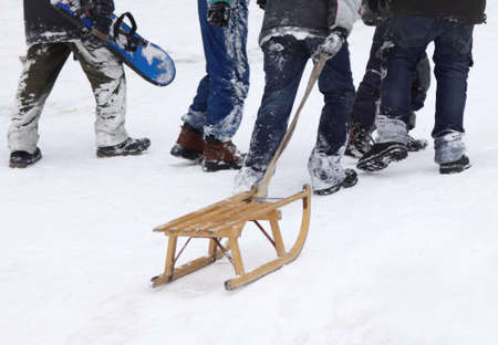 Boys climbing up the snowy hill with sledge and snowboard, focus on sledgeの写真素材