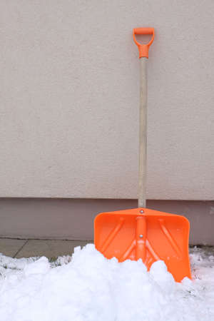 Orange plastic snow shovel against building wallの写真素材