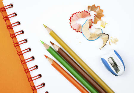 Four colorful pencils with sharpener and shavings on white notebookの写真素材