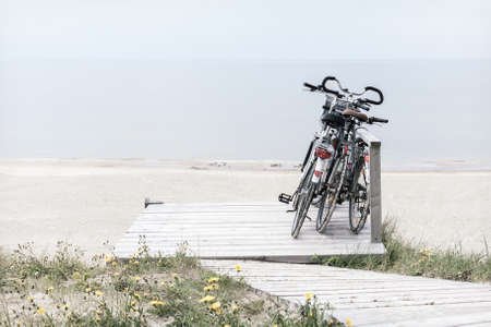 Three bicycles parked on wooden rest place by empty beach. Desaturated horizontally oriented pictureの写真素材