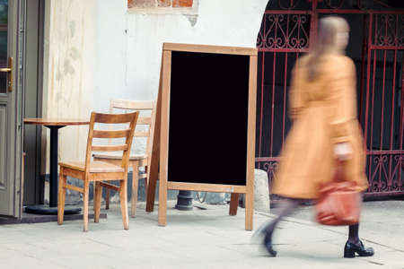 Blank restaurant blackboard on the street with blurry woman pedestrian passing byの写真素材